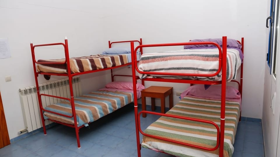 Habitación con dos literas, mesilla de madera y radiador bajo la ventana