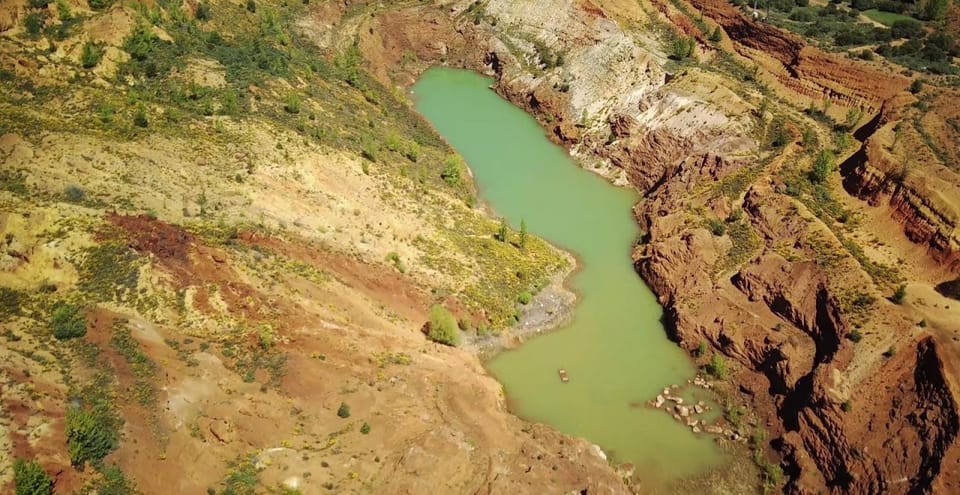 Laguna verde formada en el fondo de la antigua cantera, rodeada de taludes de tierra roja