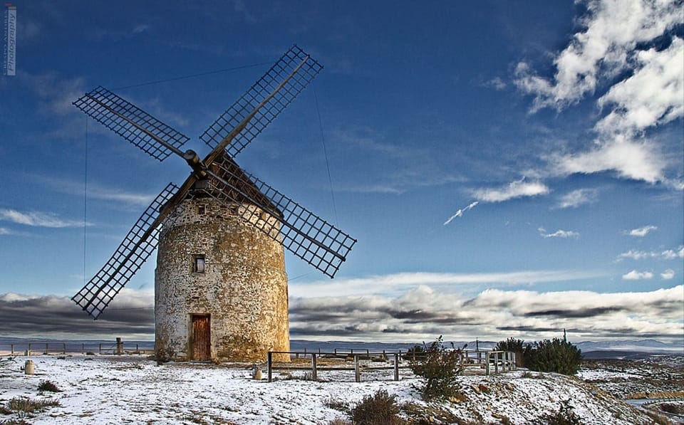 Molino de viento de piedra con las aspas de madera, sobre un llano con restos de nieve